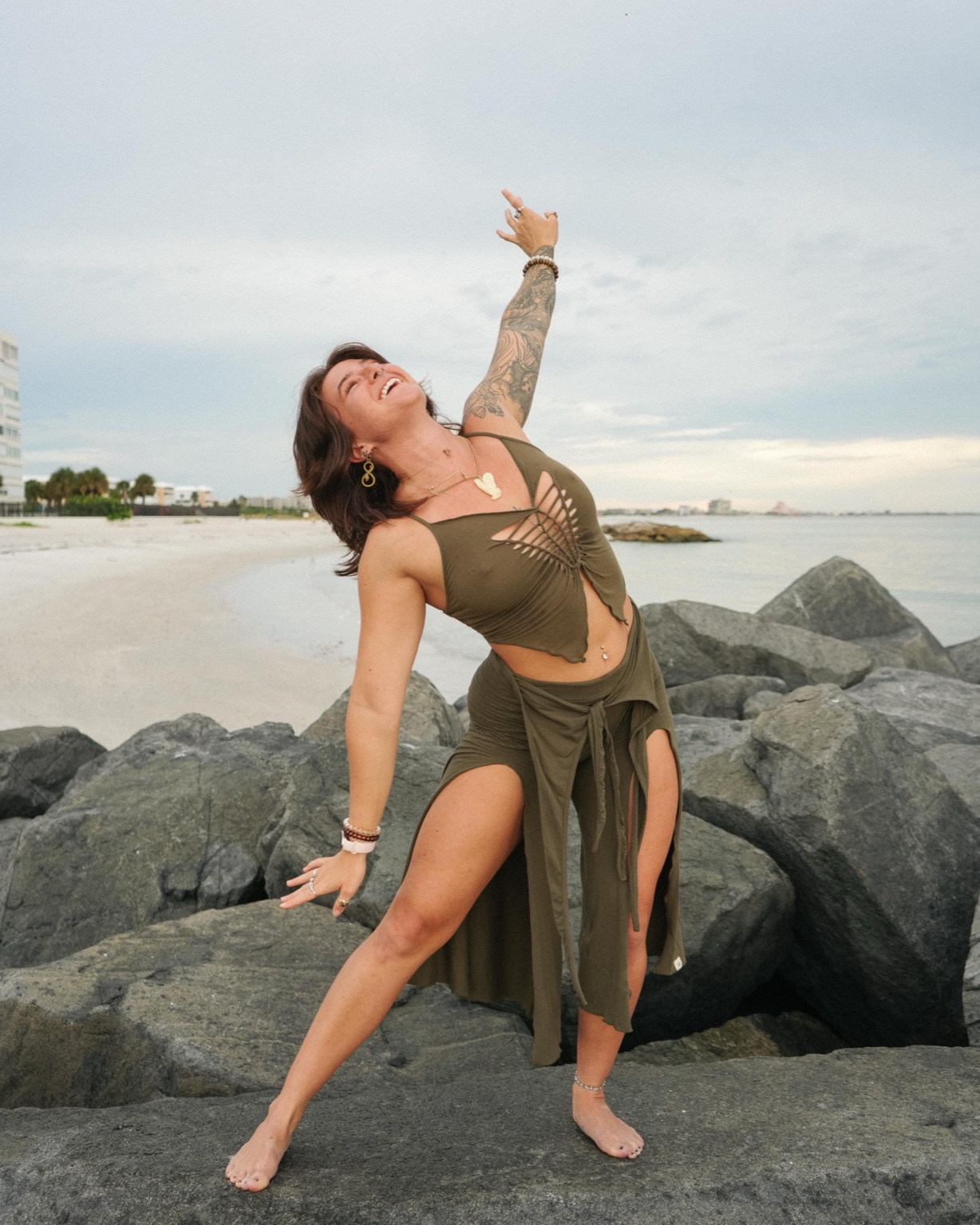 Megan Nardi laughing mid-movement on the rocks by the water, one arm reaching skyward