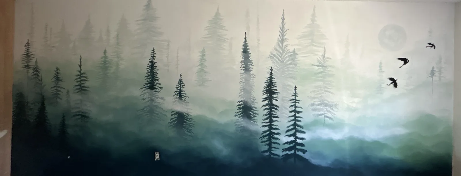 A misty evergreen forest painted across a whole bedroom wall — firs dissolving into fog, a pale moon, and three birds in flight.