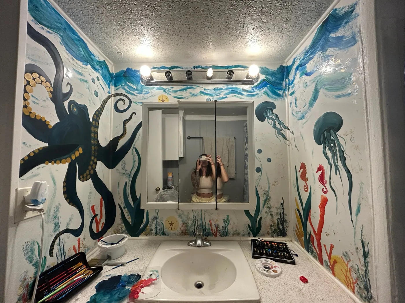A small bathroom painted as an underwater reef — an octopus, a drifting jellyfish, a seahorse and kelp wrapping every wall.